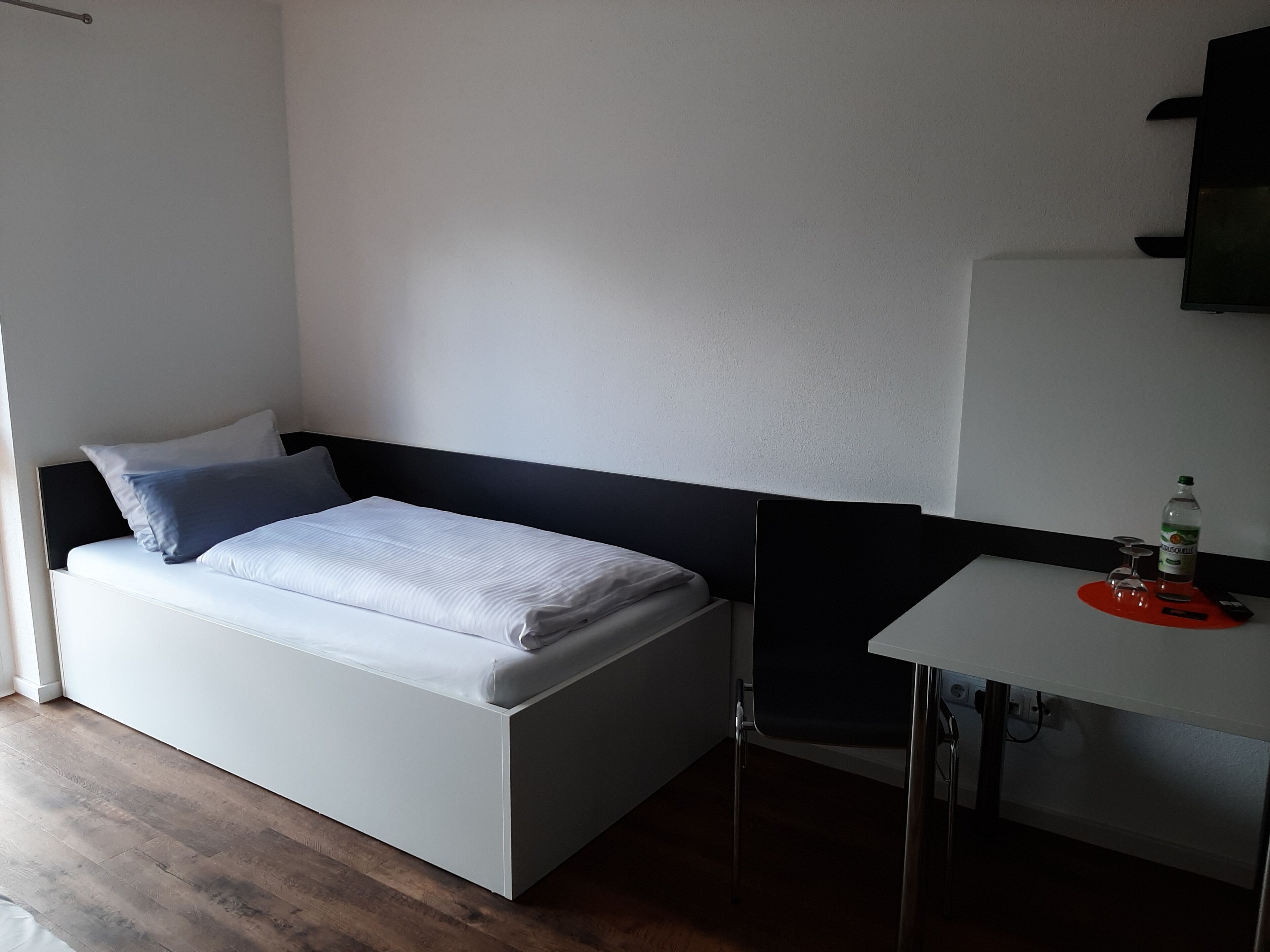 Une petite chambre moderne, équipée d’un lit, d’un bureau et d’une chaise.