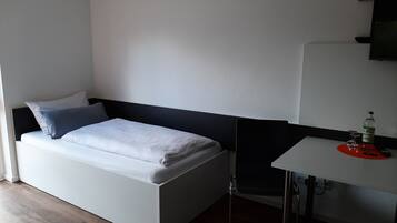 Une petite chambre moderne, équipée d’un lit, d’un bureau et d’une chaise.