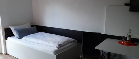 A small, modern room with a bed, a desk, and a chair.