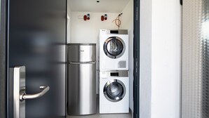 Un área de lavandería compacta con un refrigerador de acero inoxidable y dos lavadoras de carga frontal.