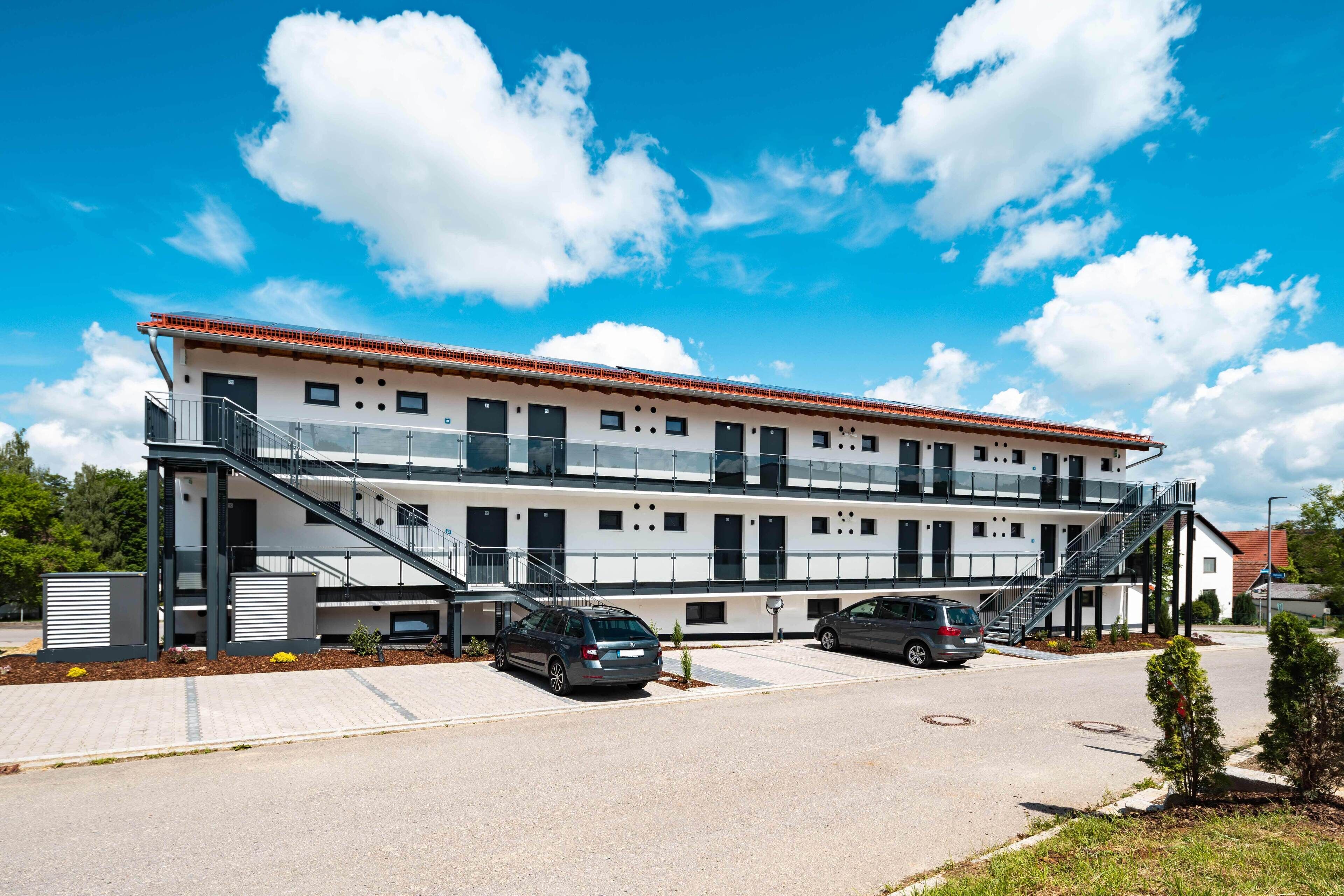 A modern multi-story building with a flat roof, large windows, and a central staircase.