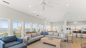 A spacious living room with a large sectional sofa, a coffee table, and a view of the ocean through large windows. - Seven Seas: Book your stay and enjoy the Island's first Splash Pad! (St. George Island)