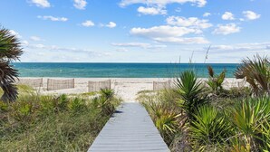 A wooden pathway leading to a sandy beach with a clear blue sky and ocean in the background. - Seven Seas: Book your stay and enjoy the Island's first Splash Pad! (St. George Island)