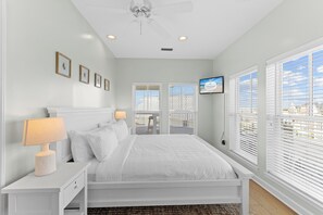 A bedroom with a bed, bedside tables, a ceiling fan, and a TV mounted on the wall.