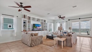 A spacious living room with a large TV, comfortable seating, and a balcony with ocean views.