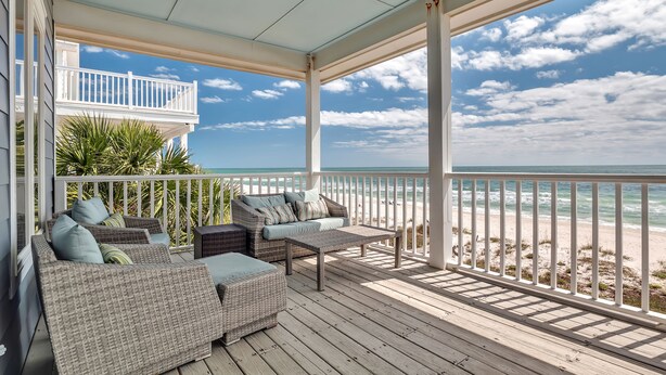 A covered outdoor seating area with wicker furniture and a view of the beach.