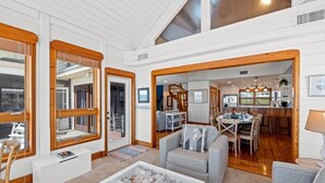 Un salón espacioso con techos altos, vigas de madera, una zona de comedor y una cocina visible a través de un arco.