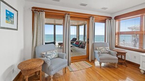 Una habitación con piso de madera, dos sillones a rayas, una mesita de mimbre y vista al mar a través de un ventanal.