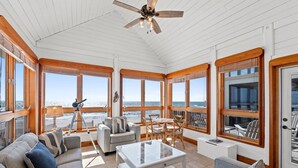 Una habitación iluminada por el sol con ventanas amplias, un ventilador de techo y un comedor con muebles de madera.