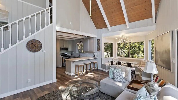 Amplia sala de estar con techo de madera, cocina con isla central y escalera con reloj.
