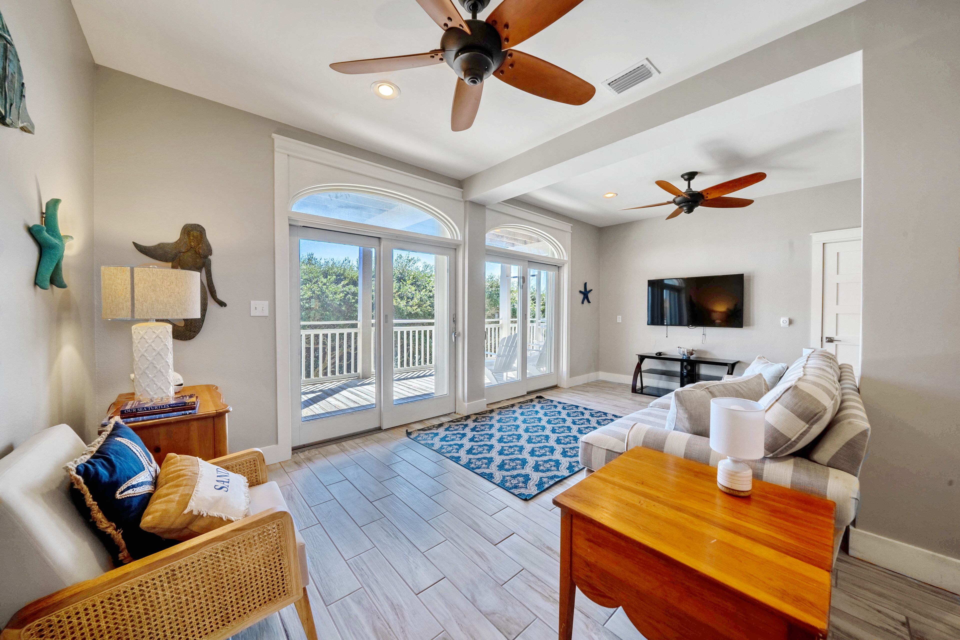 A spacious living room with a large window, a ceiling fan, a sofa, a coffee table, and a television.