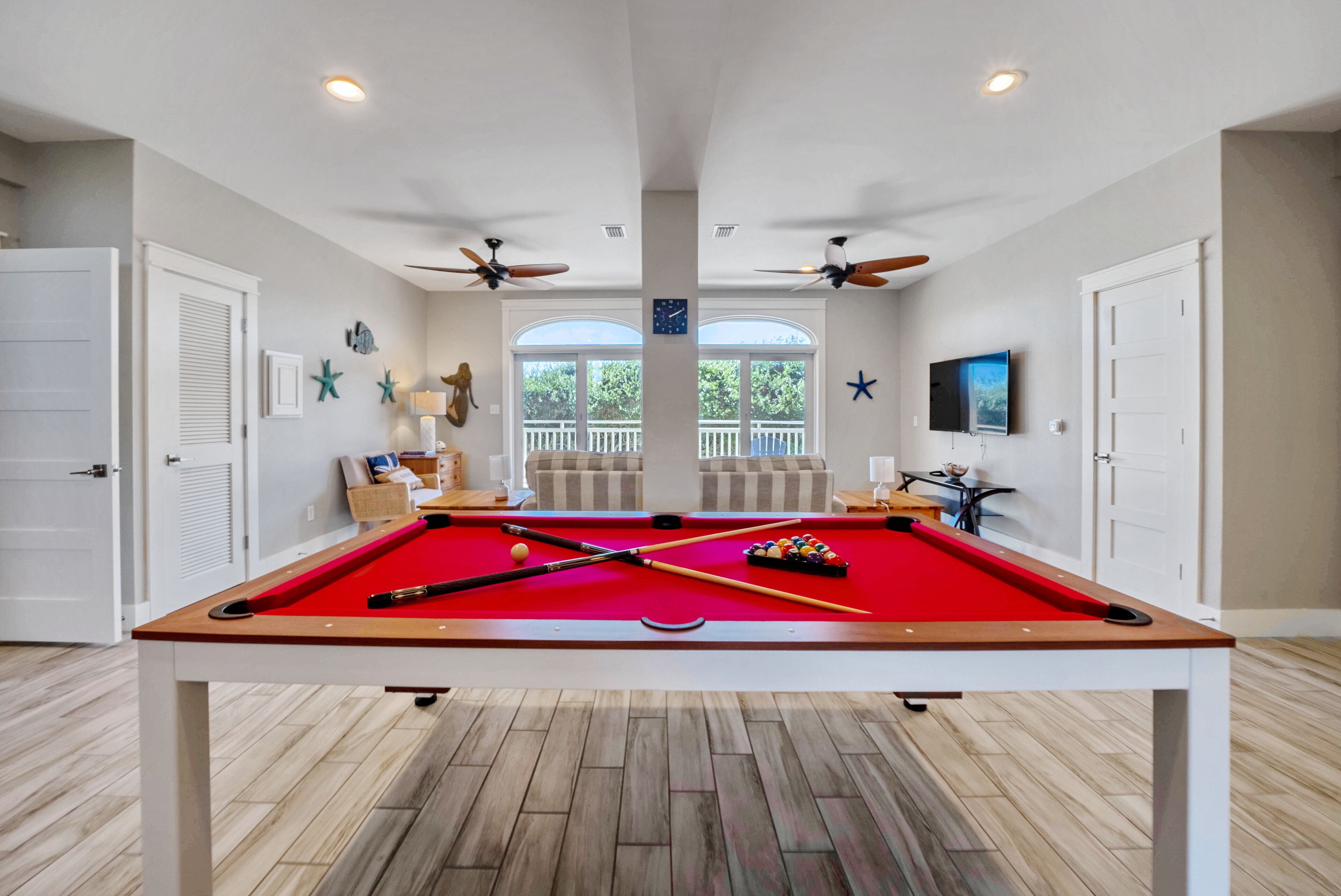 A pool table in a room with two doors, ceiling fans, and a TV mounted on the wall.