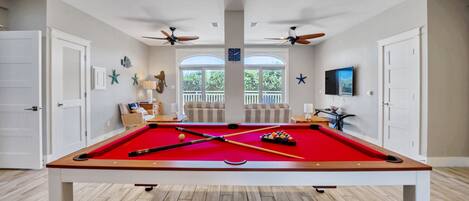 A pool table in a room with two doors, ceiling fans, and a TV mounted on the wall.