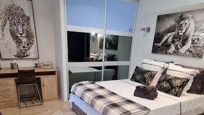 A bedroom with a bed, a desk, a chair, a large window, and artwork on the walls.