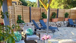 An outdoor patio with wicker furniture, a stone-tiled floor, and a wooden fence in the background.