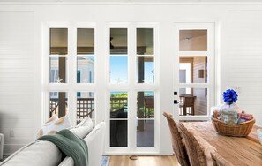 A room with a large sliding glass door leading to an outdoor area, a wicker chair, a wooden table with a basket, and a white wall with horizontal lines.