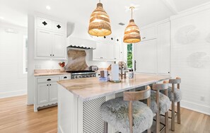 Une cuisine moderne avec des meubles blancs, un plan de travail en marbre et deux suspensions lumineuses.