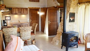 Un salon chaleureux avec une cheminée, des fauteuils en osier, un canapé et, au fond, un coin cuisine.