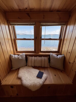 Eine Holzhütte mit integriertem Sitzplatz und zwei Fenstern mit Blick auf ein Gewässer.