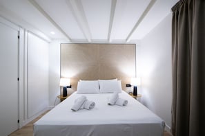 A modern hotel room with a large bed, two bedside tables with lamps, a headboard with a geometric pattern, and a wardrobe.