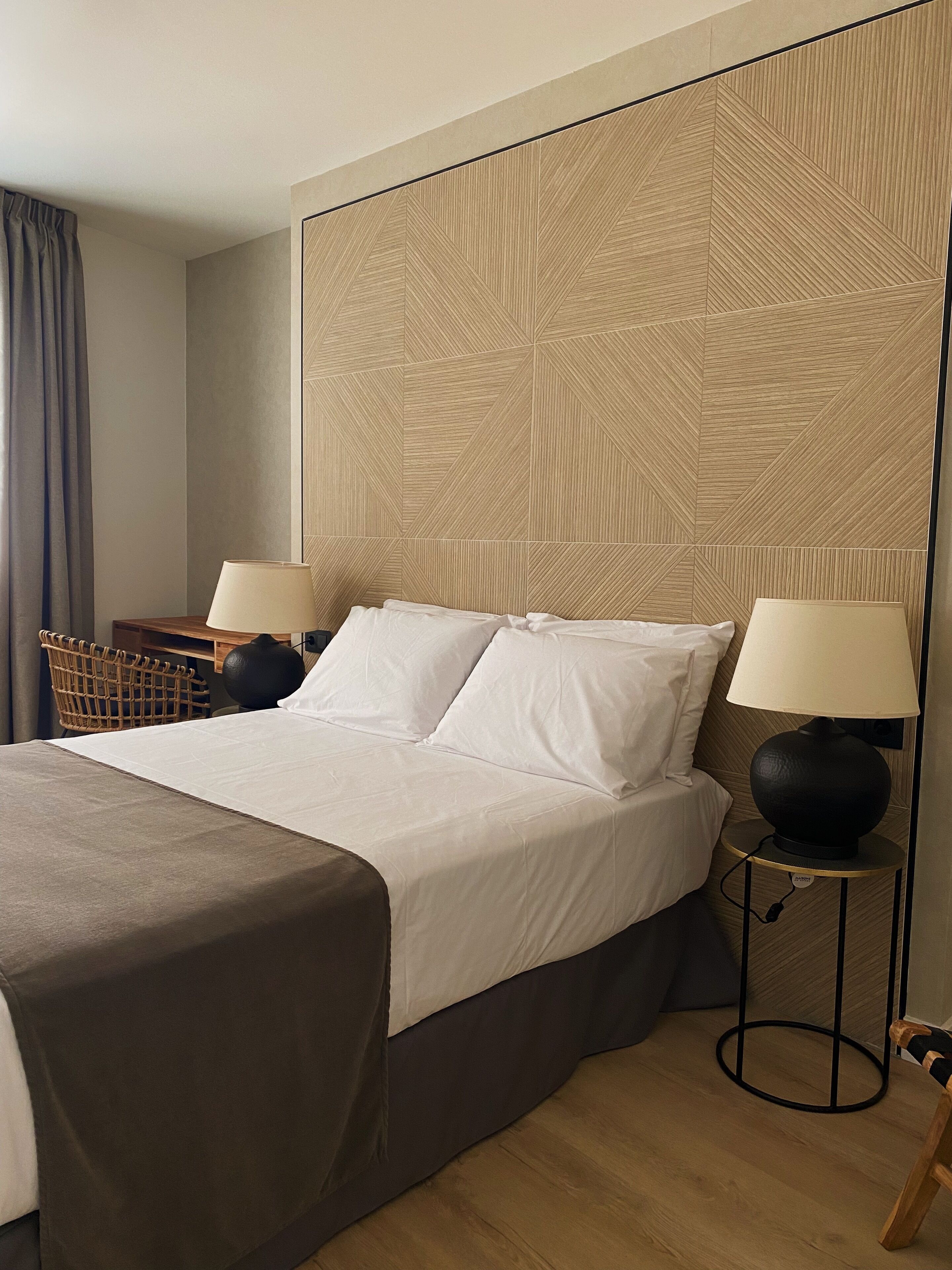 A hotel room with a large bed, two bedside tables with lamps, a wicker basket, and a wooden chair.
