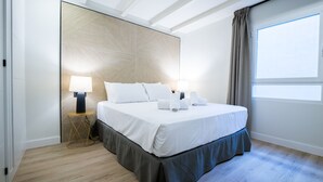 Une chambre d’hôtel moderne avec un grand lit, des lampes de chevet, une tête de lit en bois et une grande fenêtre avec des rideaux.