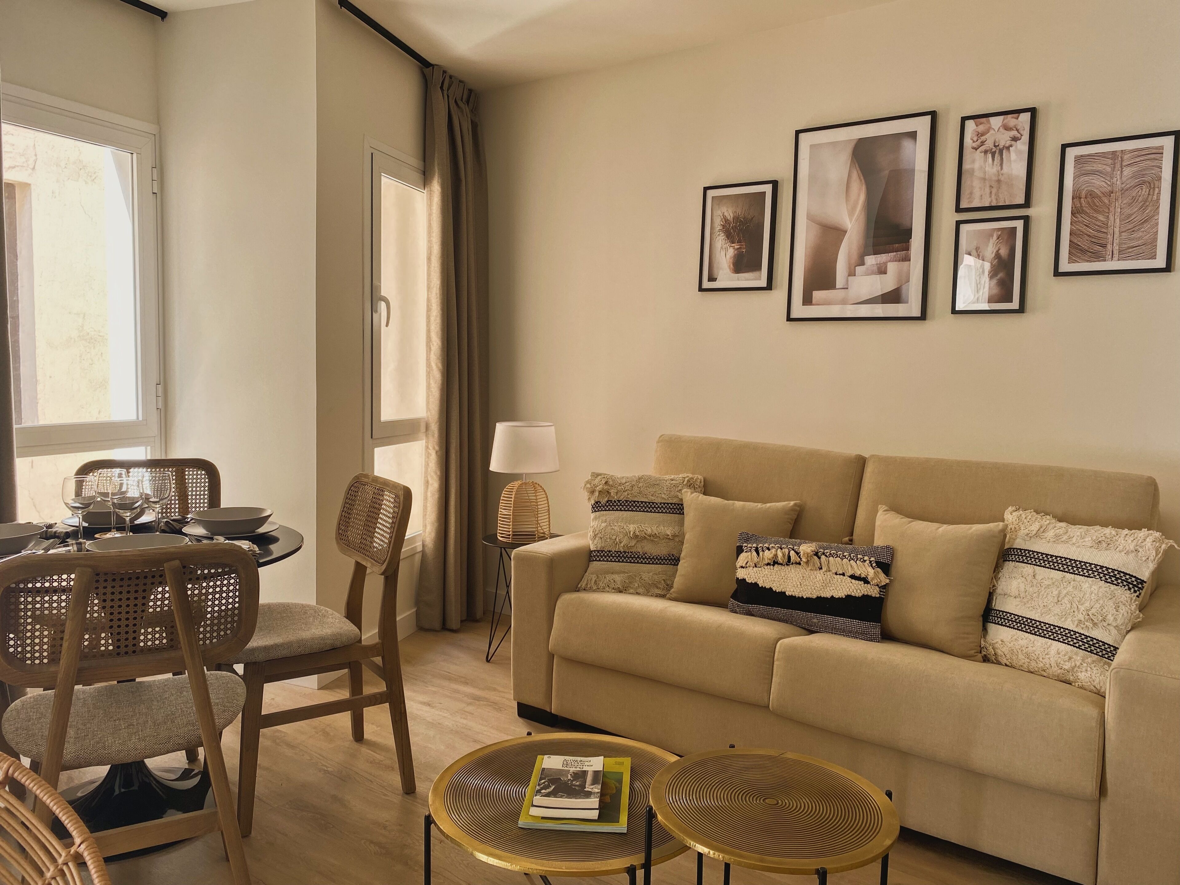 A living room with a beige sofa, two round tables, a dining table with chairs, and a window with curtains.
