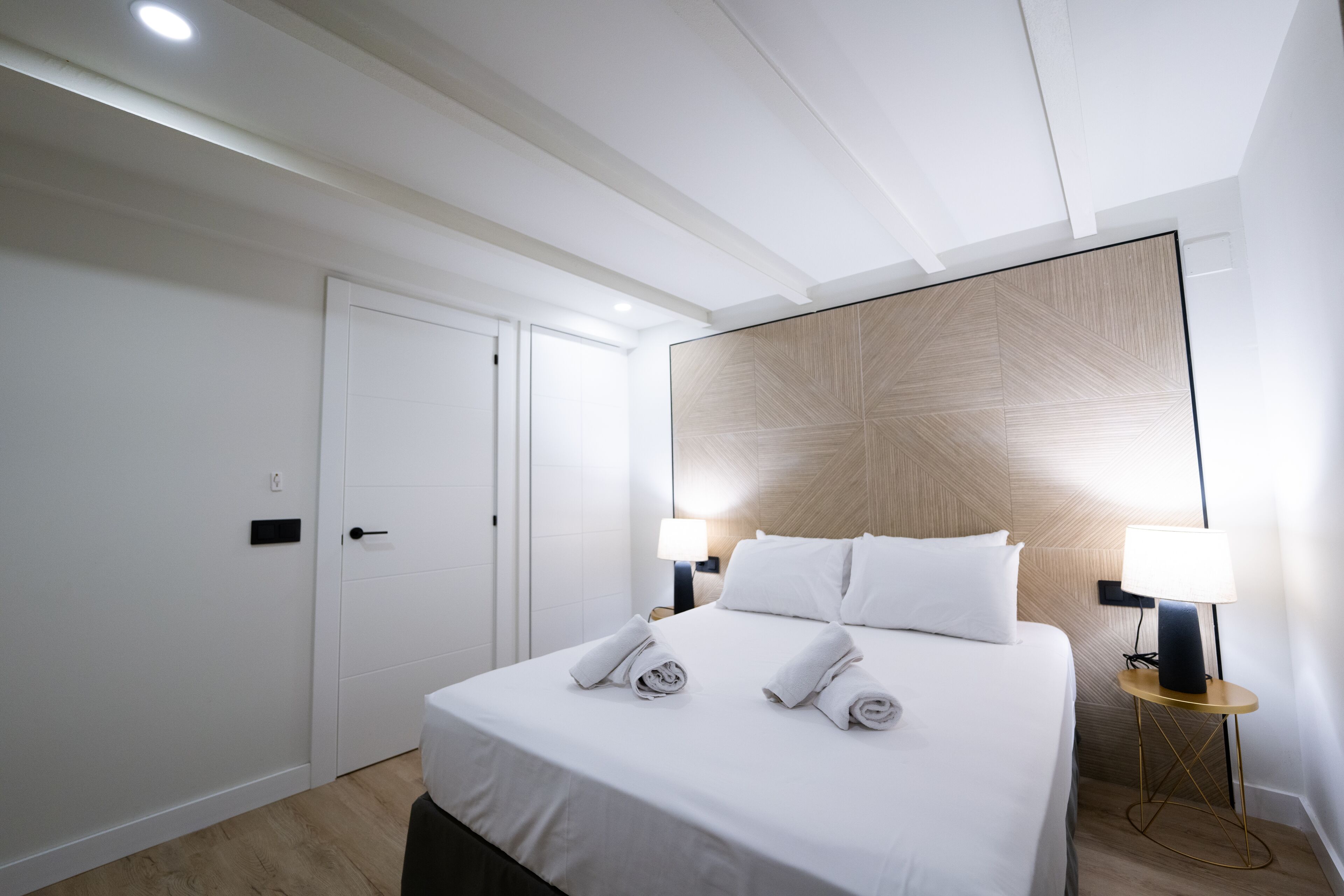A hotel room with a neatly made bed, two bedside lamps, and a large wall panel.