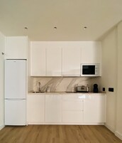 Une cuisine moderne avec des meubles blancs, un four à micro-ondes encastré, un grille-pain et un réfrigérateur.