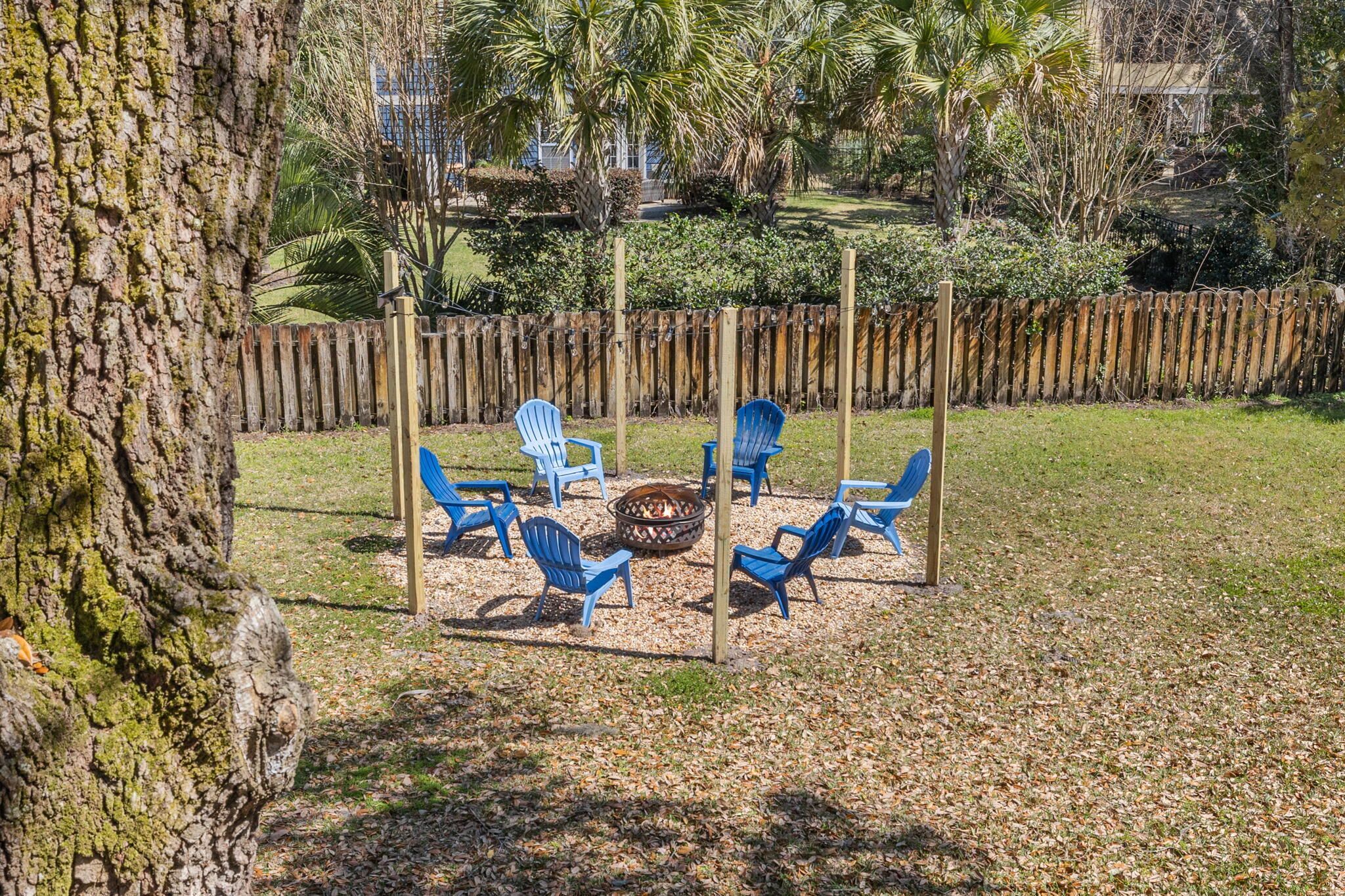A fire pit with blue chairs arranged around it in a backyard setting.