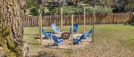 A fire pit with blue chairs arranged around it in a backyard setting.