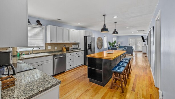 A modern kitchen with white cabinets, a wooden island, and a dining area with blue bar stools. - Beach house w/ FREE Golf Cart & Fire Pit! (Pawleys Island)