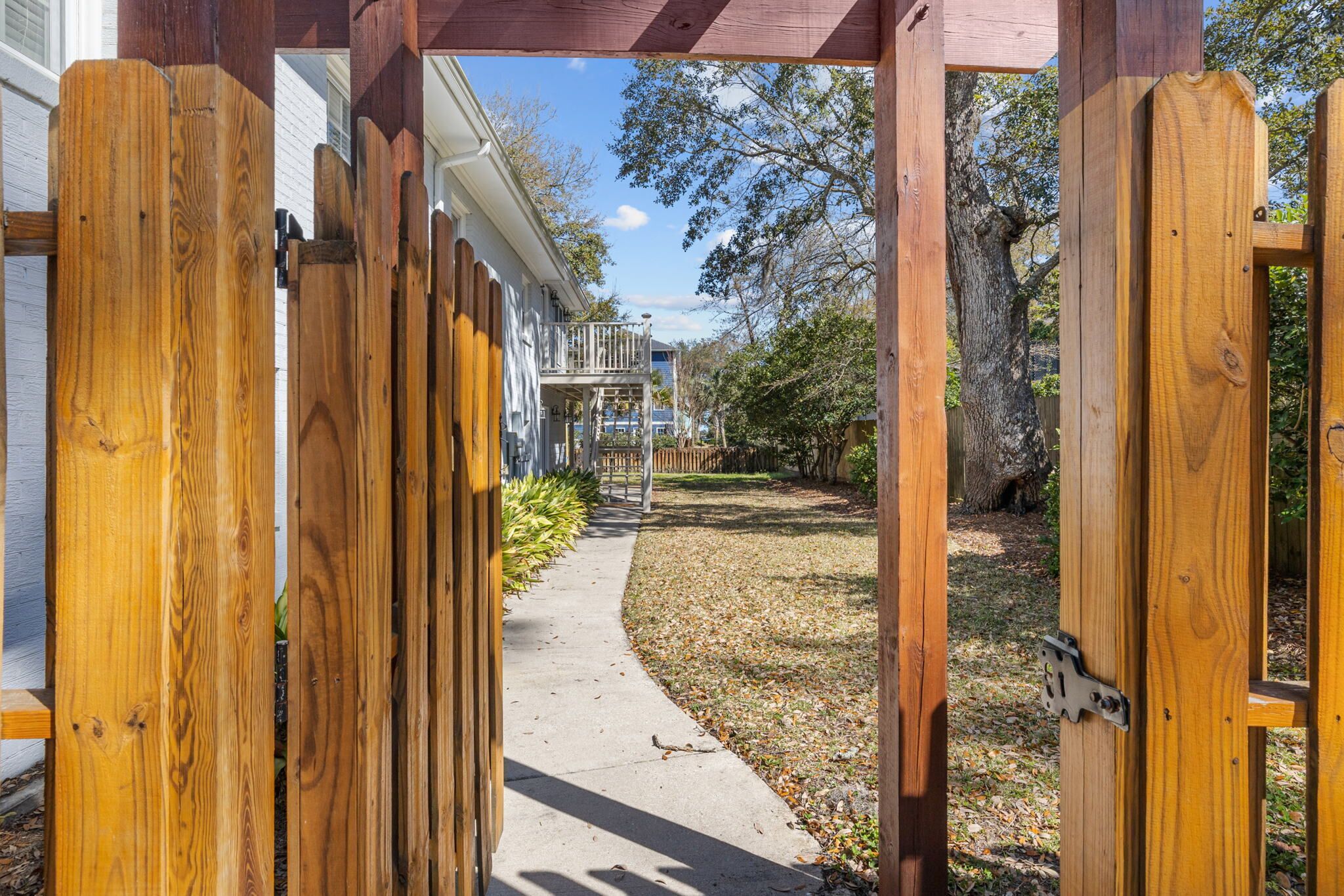 A wooden gate leading to a pathway with a house in the background.