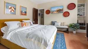 Un dormitorio con cama, banca, planta y adornos en la pared.