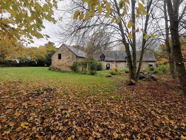 A stone building with a grassy yard and fallen leaves.