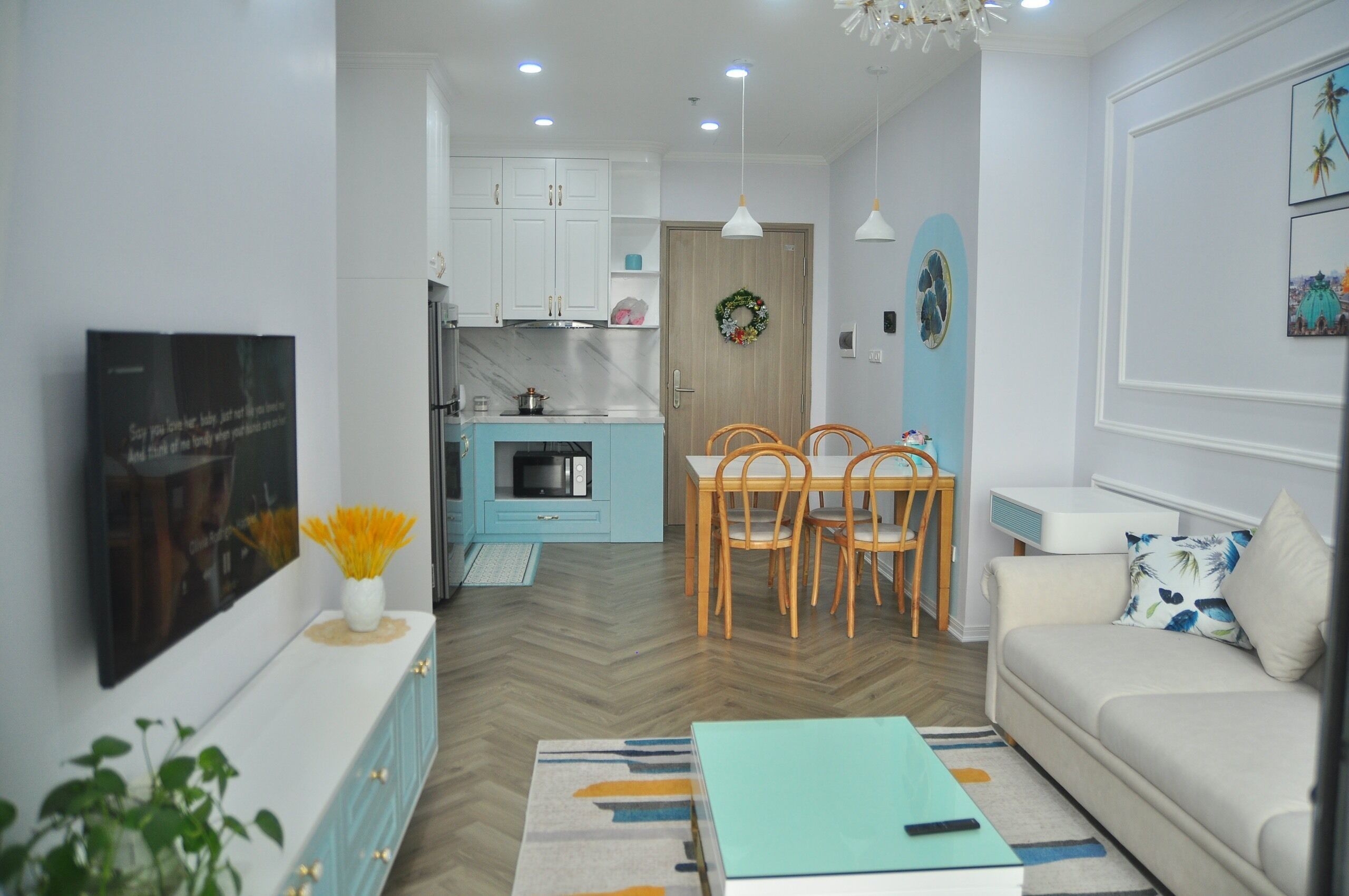 Un salon moderne avec un canapé, une table basse et un téléviseur. On y trouve également un coin repas avec une table et des chaises. La cuisine est visible et se distingue par ses armoires blanches et son four à micro-ondes.