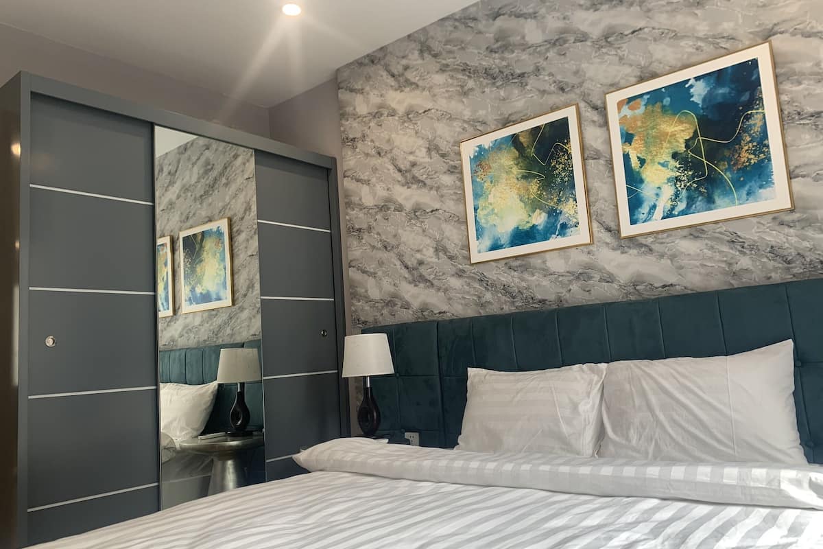 Een moderne slaapkamer met een groot bed, een wand met marmerlook en twee abstracte schilderijen.