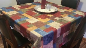 Uma mesa de jantar com toalha de mesa de colcha colorida, rodeada por cadeiras de madeira.