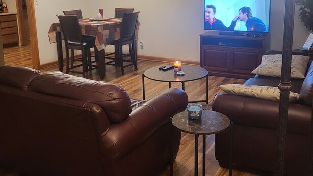 Uma sala de estar com um sofá de couro marrom, uma mesa de jantar com cadeiras, uma televisão e um abajur.