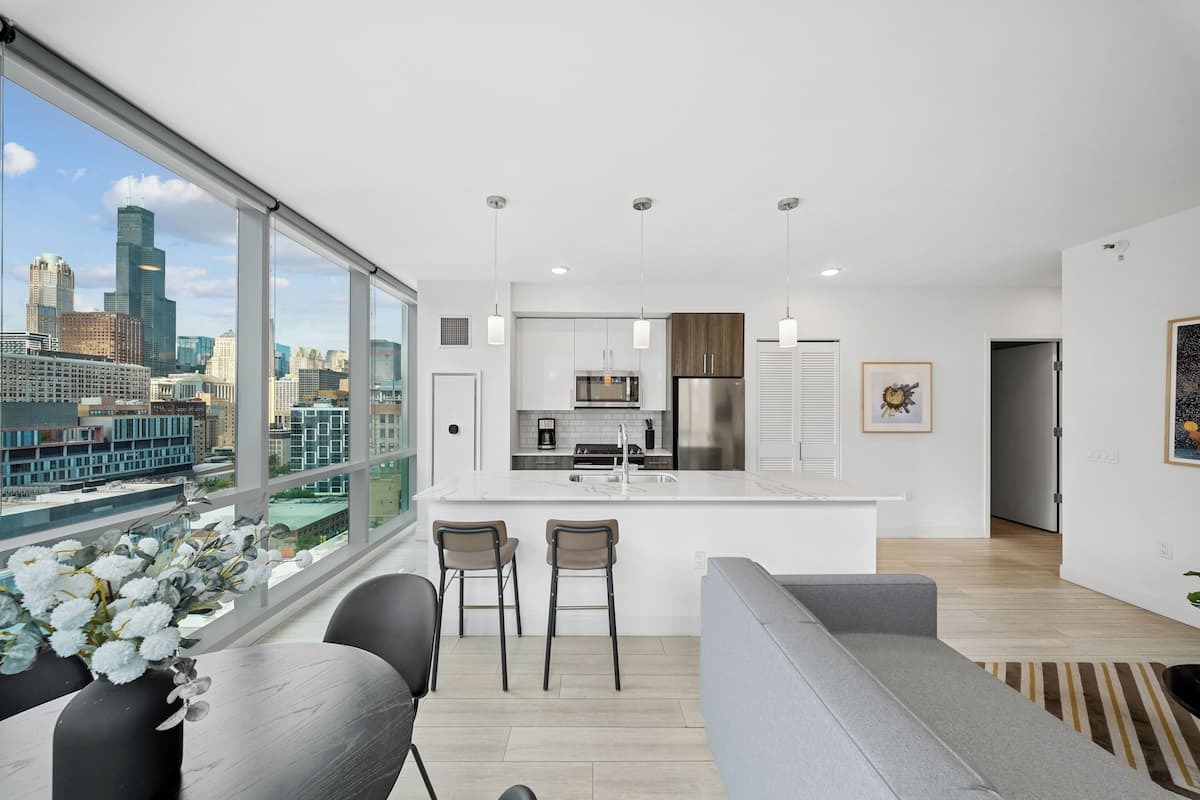 A modern kitchen with a large island, bar stools, and a view of a cityscape through large windows.