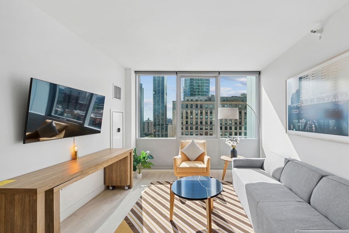A modern living room with a large window, a flat-screen TV, a sofa, a coffee table, and a console table.