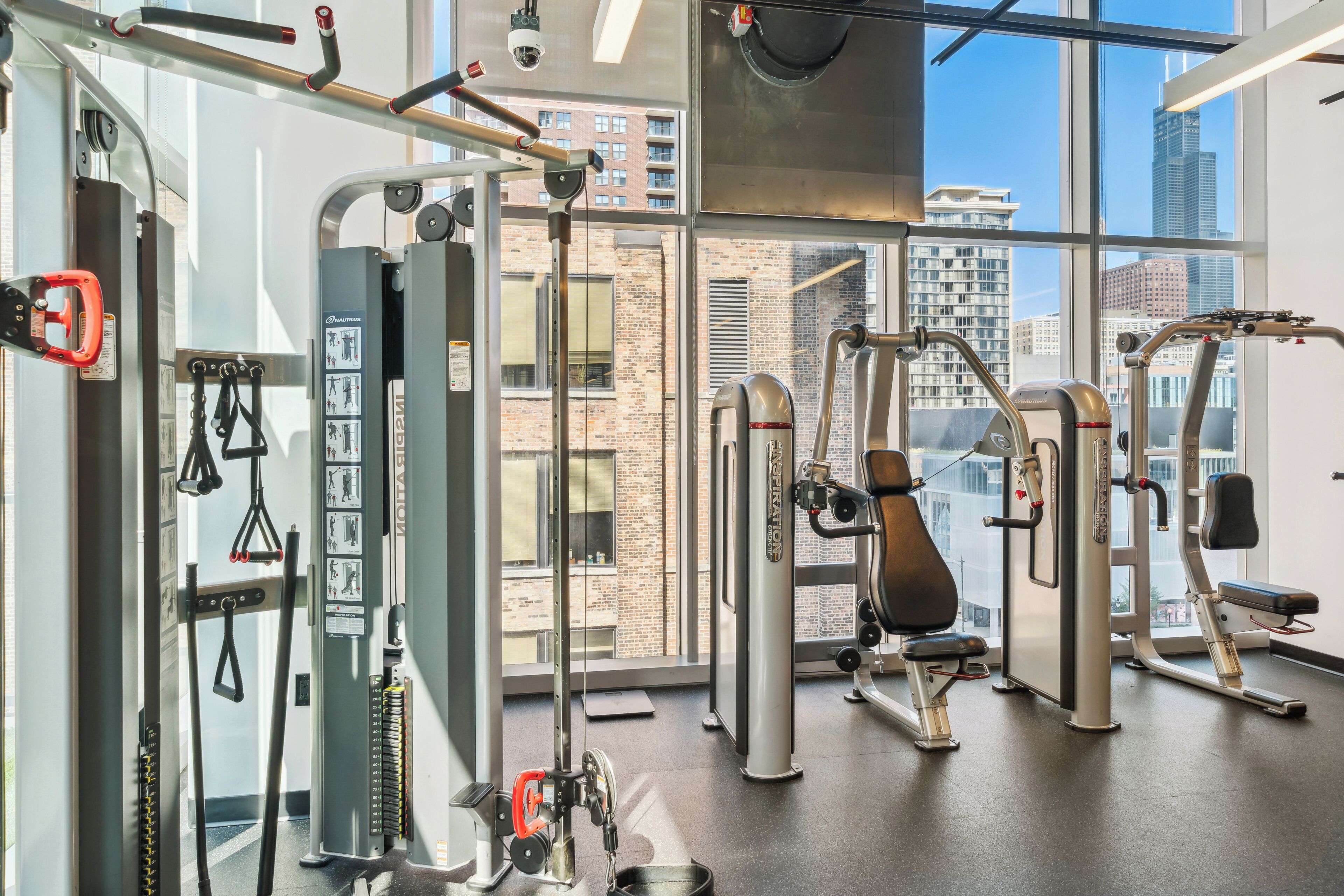 A gym with various exercise equipment, large windows, and a view of city buildings.