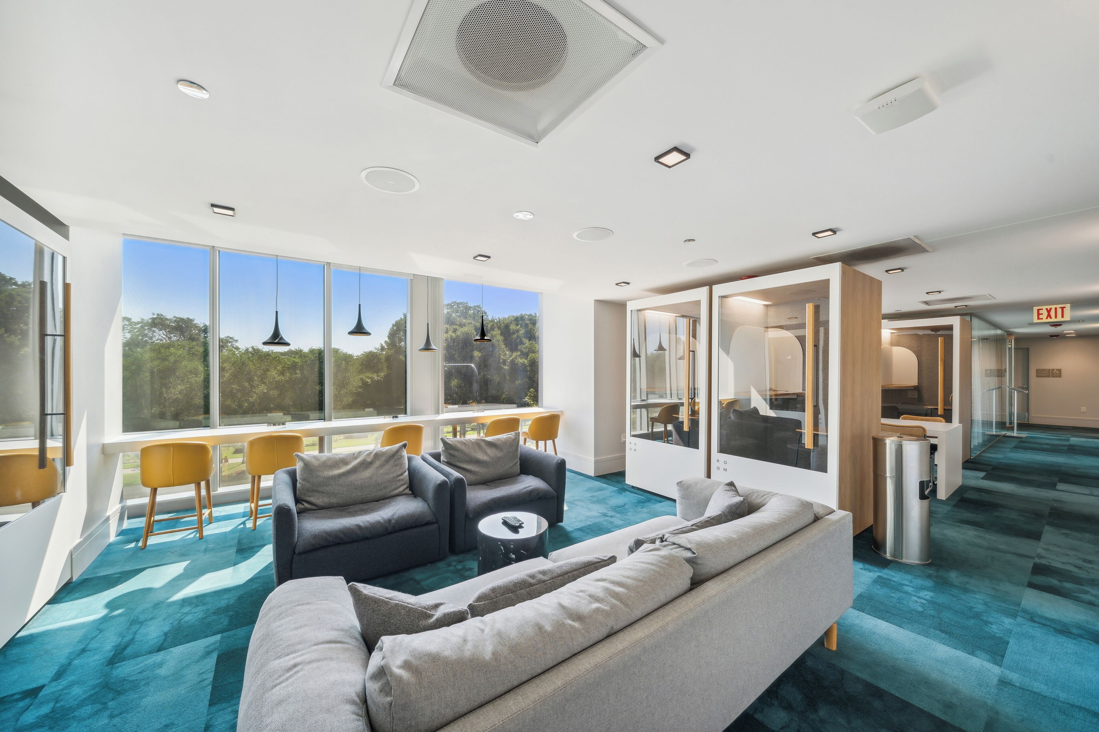 A modern lounge area with a large window, a sofa, a coffee table, and a dining area with yellow chairs.