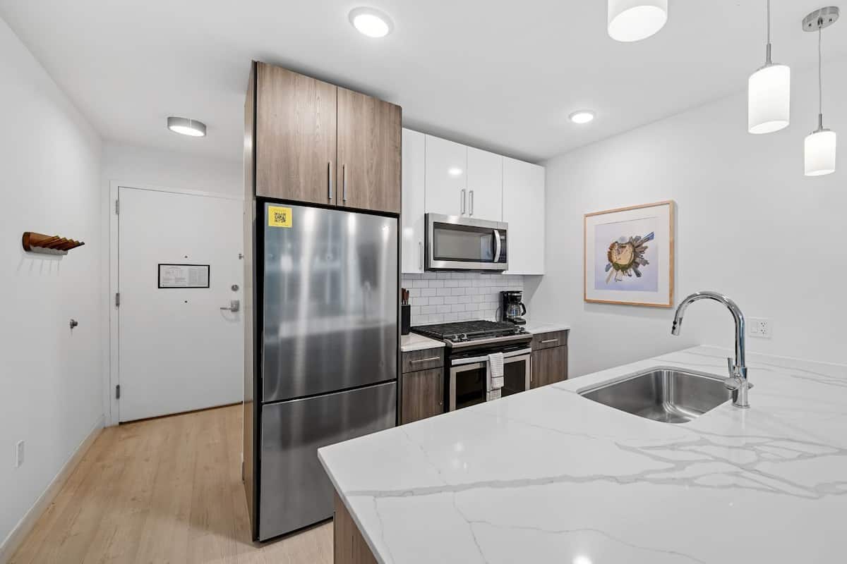 A modern kitchen with stainless steel appliances, a marble countertop, and pendant lighting.