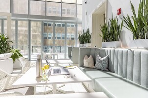 Un espacio interior moderno y bien iluminado con una mesa blanca, un sofá gris y plantas en macetas.