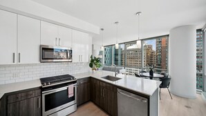 A modern kitchen with a built-in microwave, stove, and dishwasher, large windows with city views, and a dining area with a table and chairs. - Sentral Michigan Avenue (Chicago)