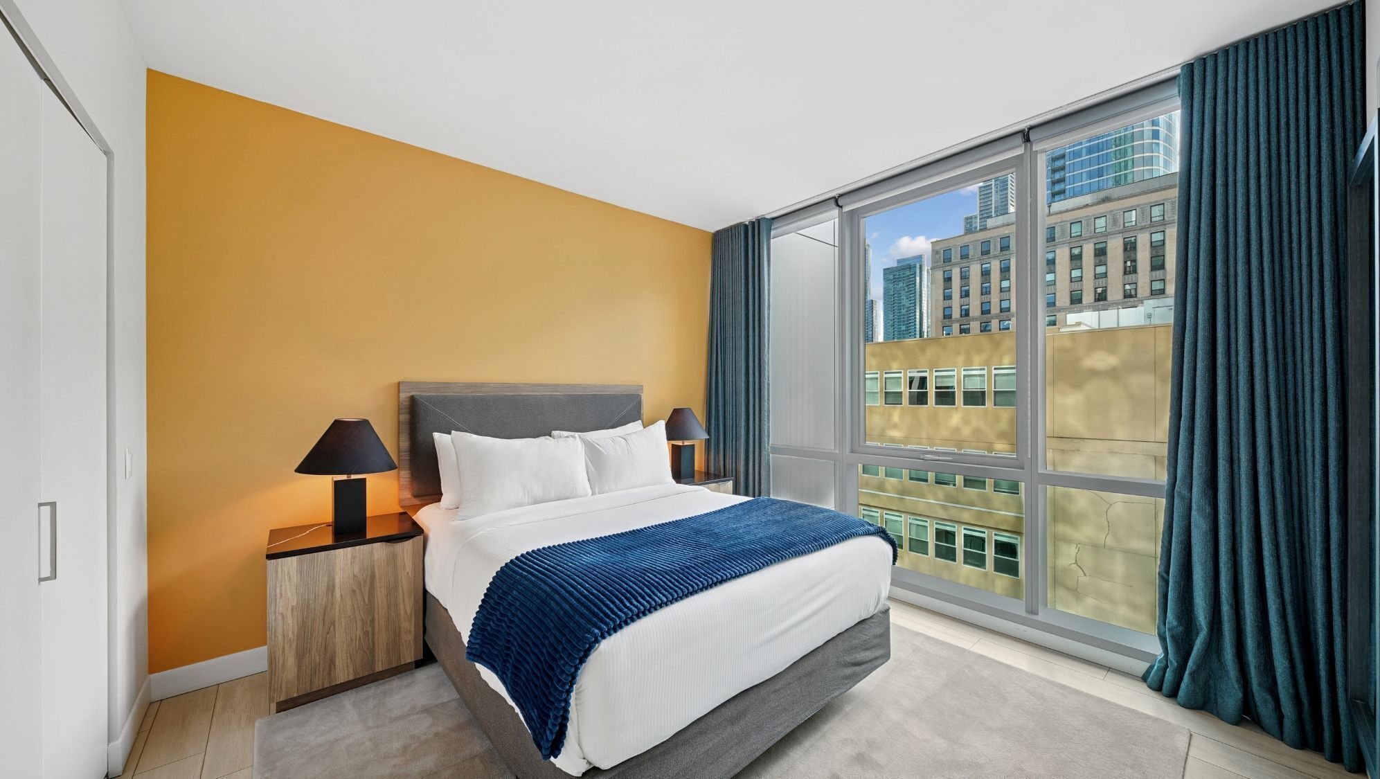 A hotel room with a large window, a bed, a nightstand, and a lamp.