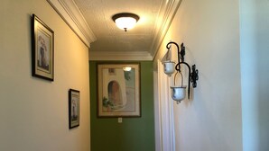 Een gang met groene wanden, kunstwerken in lijsten, een plafondlamp en wandlampen.