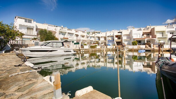 Un port esportiu amb barques amarrades, envoltat d'edificis blancs amb balcons, sota un cel blau i clar.