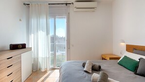 Un dormitori amb un llit, una tauleta de nit, un armari, una finestra amb cortines i un aparell d'aire condicionat.
